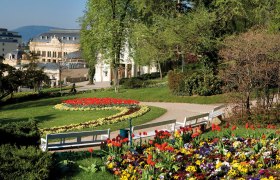 Kurpark Baden mit bl&uuml;henden Blumenbeeten, B&auml;nken und einem historischen Geb&auml;ude im Hintergrund.