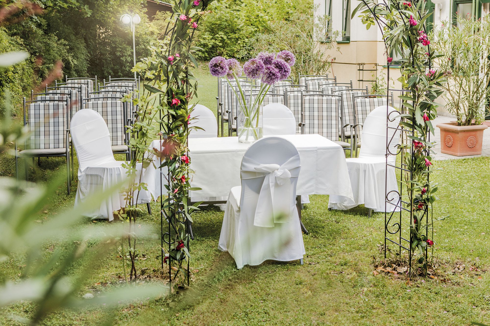 Festlich geschmückter Garten im Hotel Höldrichsmühle. Um einen weißen Tisch sind Stühle mit Hussen angereiht. Ein Hochzeitsbogen dekoriert die Umgebung.