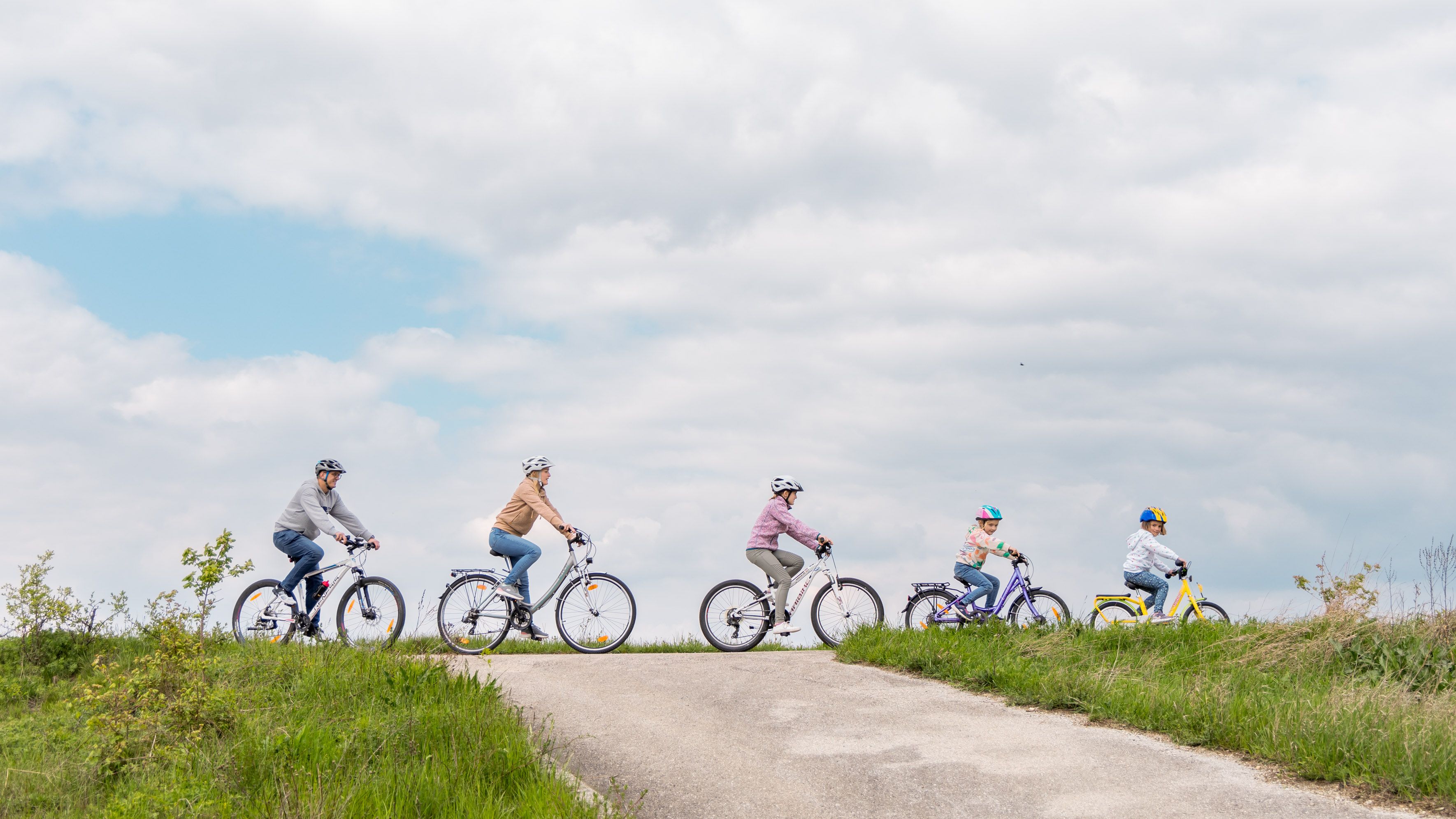 Fünfköpfige Familie radelt hintereinander zusammen entlang eines geraden Radweges im Wienerwald. 