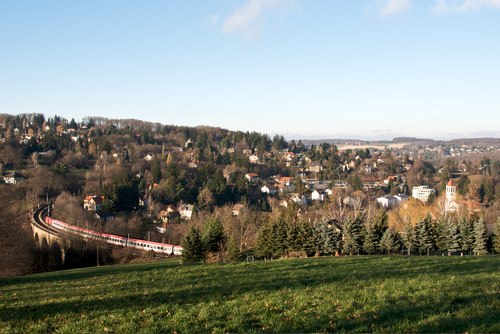 Landschaft mit Zug auf Viadukt in Eichgraben, umgeben von Hügeln und Häusern.