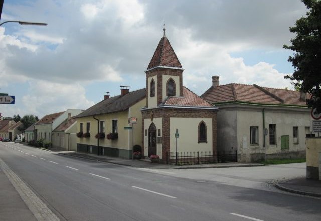 Straße in Lanzendorf mit Kirche und Wohnhäusern.