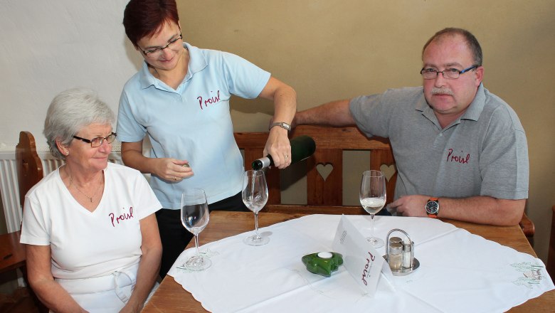 Three people are sitting at a table, a woman is pouring wine.