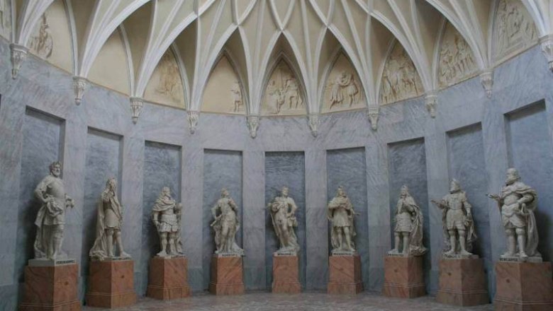 Interior view of the Habsburg Hall with statues on pedestals and a vaulted ceiling pattern.