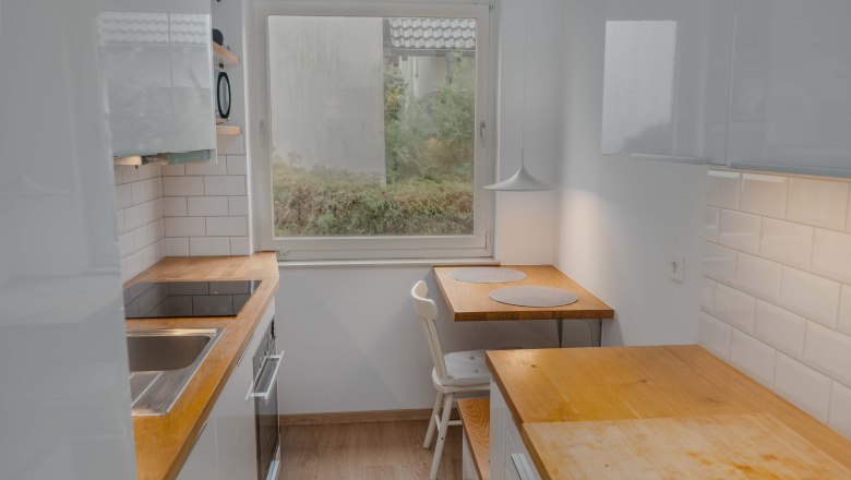 Kleine Küche mit Holzarbeitsplatten, einem Fenster und einem kleinen Esstisch mit zwei Platzdecken