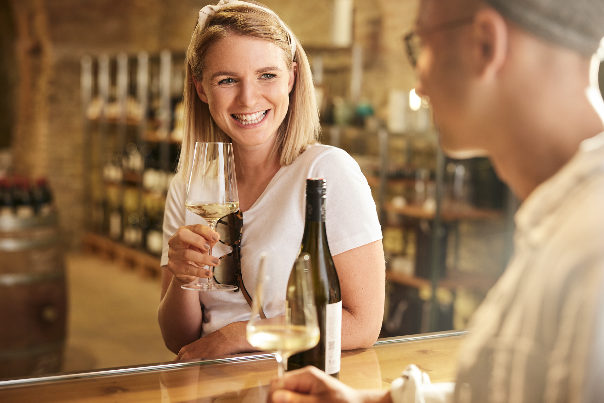 In einer einladenden Atmosphäre genießen zwei Freunde ein Glas Wein, während sie sich angeregt unterhalten. Die warmen Farben des Raumes und die Regale voller erlesener Weine schaffen eine perfekte Kulisse für entspannte Stunden. Hier wird die Freude am Leben und die Geselligkeit zelebriert.