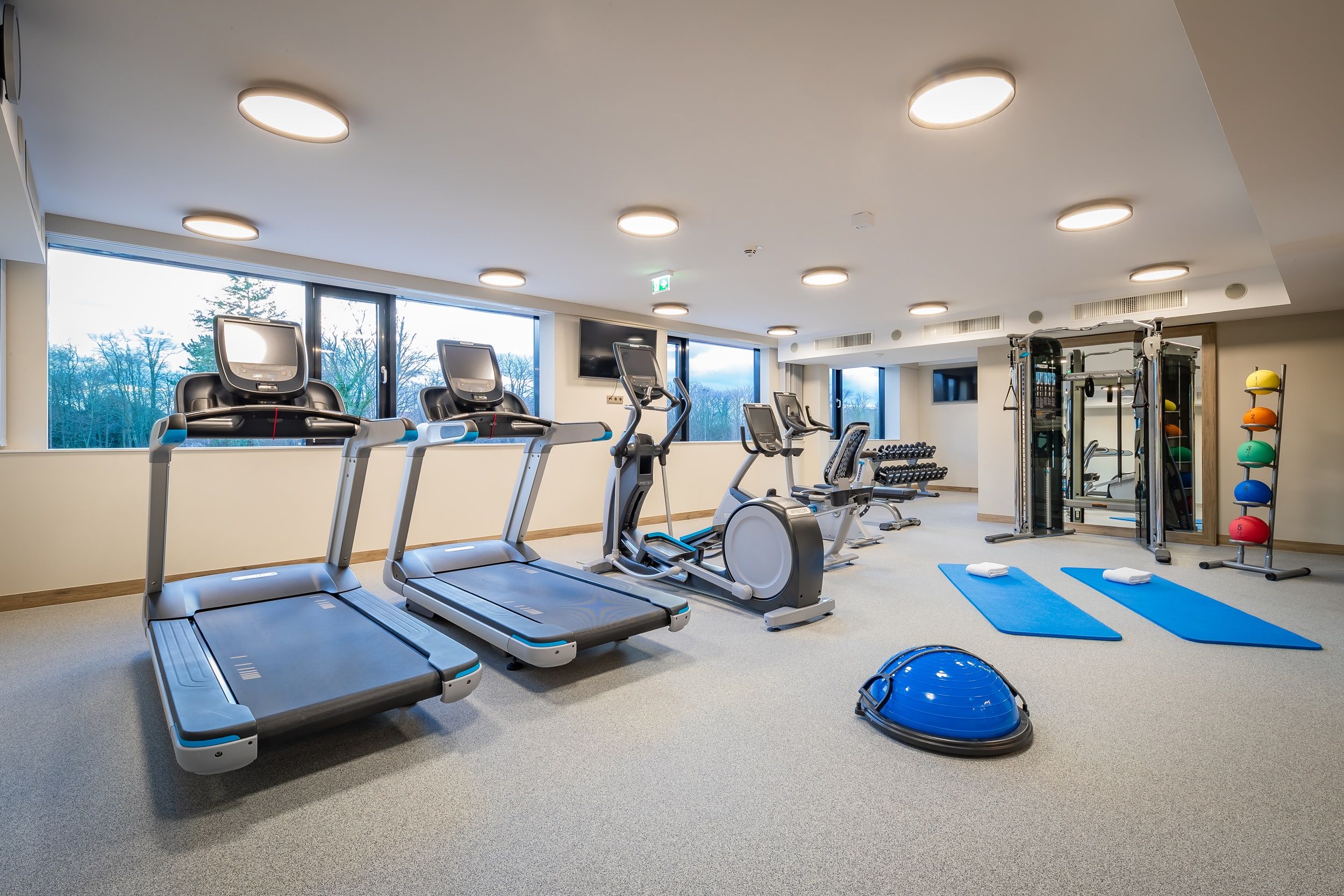 Fitnessraum mit Laufbändern, Crosstrainer, Hanteln und Gymnastikmatten.