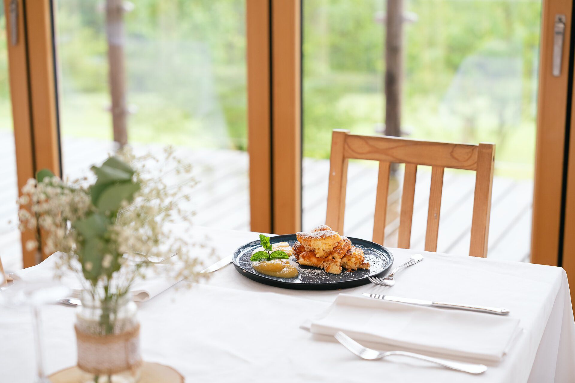 Fein angerichteter Mirli-Schmarrn auf einem weiß gedeckten Tisch, umgeben von Holzstühlen und natürlichem Licht.