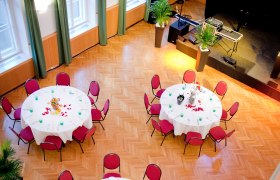 A festively decorated hall with round tables and red chairs, view from above.