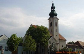 Church in Moosbrunn with green church tower and surrounding buildings.