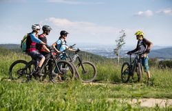 In der warmen Sommerluft versammeln sich Mountainbiker auf einem malerischen Pfad, umgeben von üppigem Grün und atemberaubenden Ausblicken. Die Vorfreude auf das Abenteuer in den sanften Hügeln des Wienerwaldes ist spürbar, während die Gruppe sich auf den nächsten Abschnitt ihrer Tour vorbereitet.