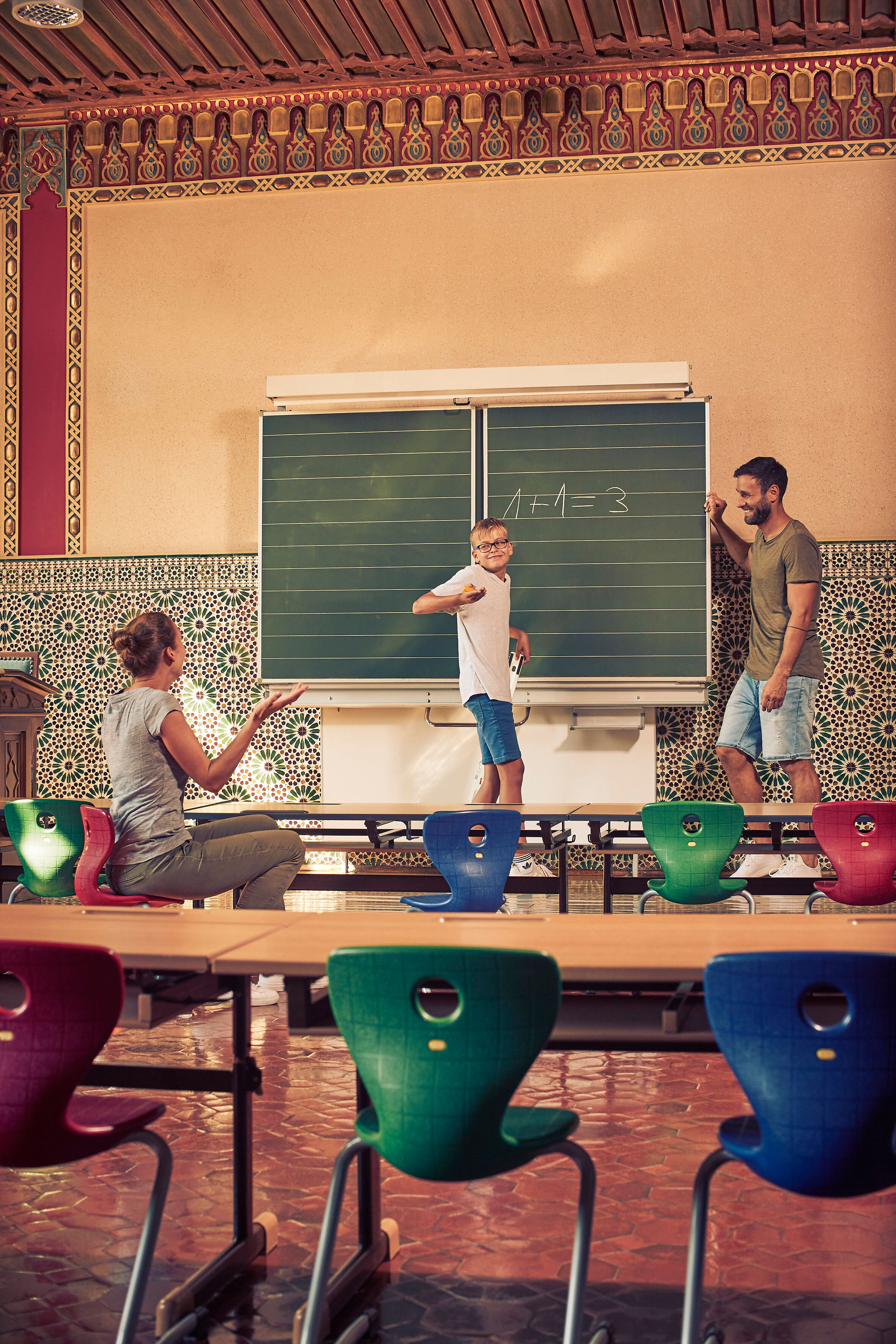 In einem einladenden Klassenzimmer voller Farben und Kreativität wird das Lernen zum Abenteuer. Eine Familie genießt die Zeit miteinander, während sie spielerisch Wissen vermittelt. Die harmonische Atmosphäre lädt dazu ein, die Schönheit der Natur und die Freude am gemeinsamen Entdecken zu erleben.