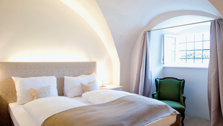 Gemütliches Schlafzimmer mit Doppelbett, grünem Sessel und gewölbter Decke.