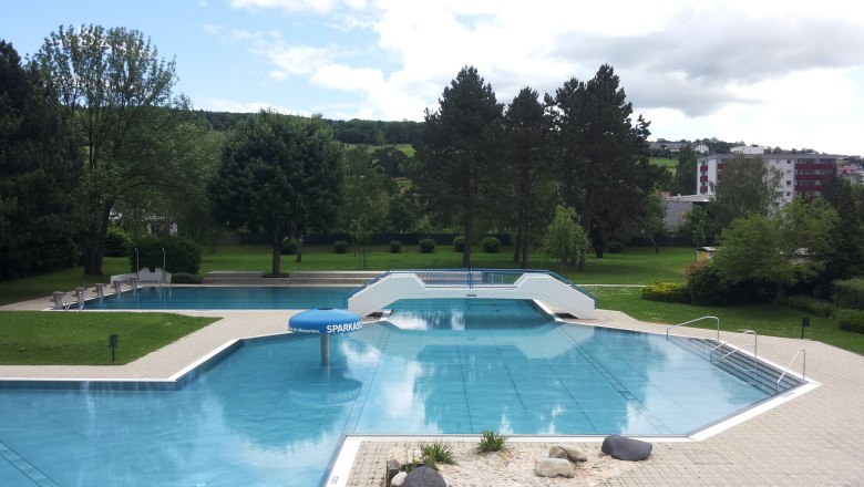An empty outdoor pool with several pools, surrounded by trees and lawns, under a cloudy sky.