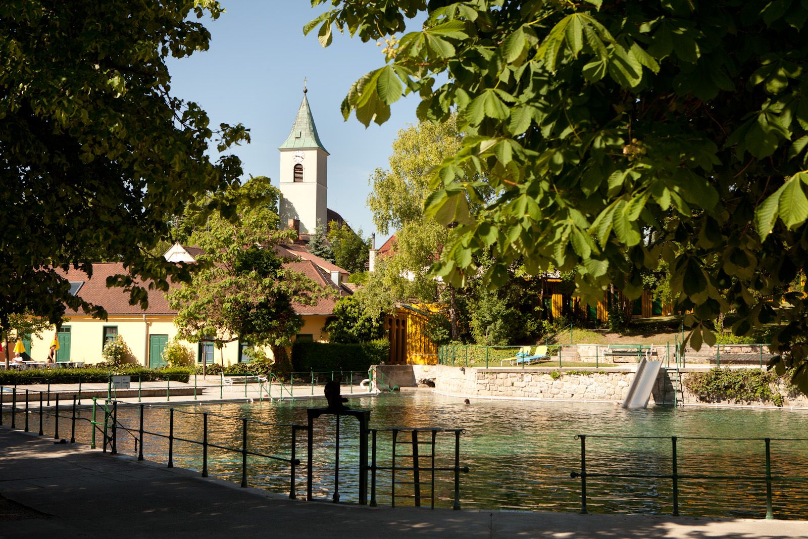 Thermalbad Bad Fischau-Brunn mit Kirche im Hintergrund, umgeben von Bäumen.