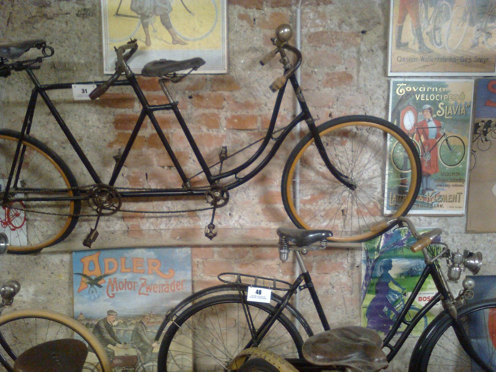 Alte Fahrräder und Vintage-Poster an einer Backsteinwand im Fahrradmuseum Schloss Vösendorf.