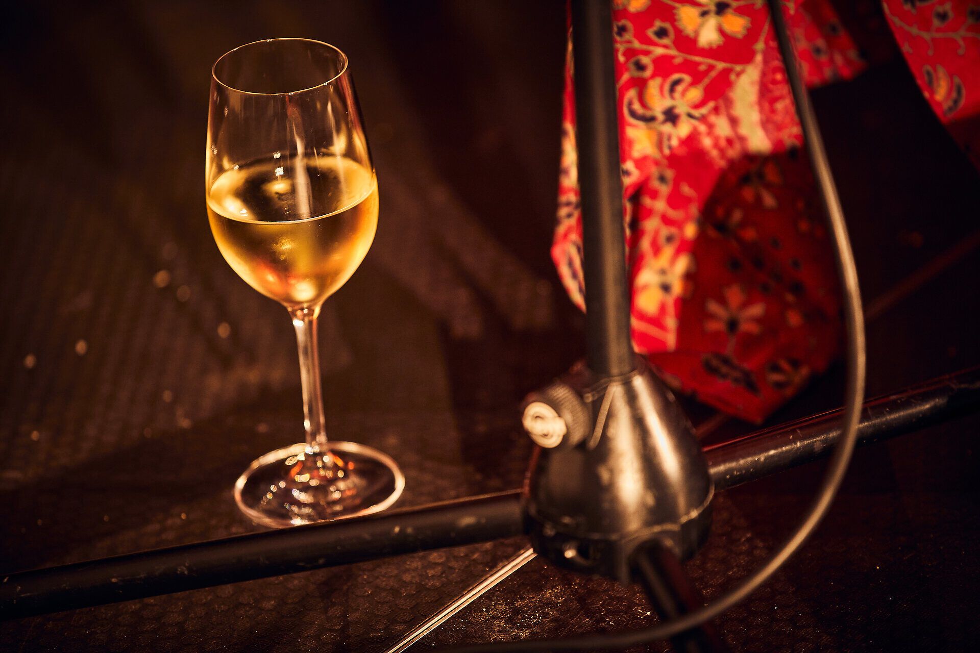 Ein elegantes Glas mit goldenem Wein steht auf dem Boden, umgeben von der warmen Atmosphäre eines kulturellen Events. Die sanften Lichter und die festliche Stimmung laden dazu ein, die köstlichen Aromen der Region zu genießen und unvergessliche Momente zu erleben.