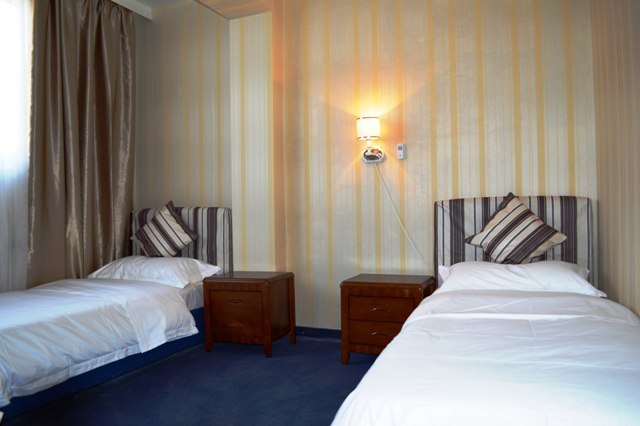 A hotel room with two single beds, bedside tables and a wall lamp.
