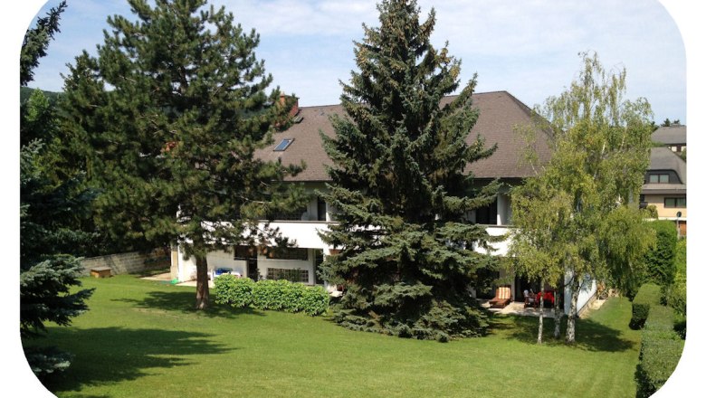 Rückansicht eines Gasthofs mit Garten und Bäumen.