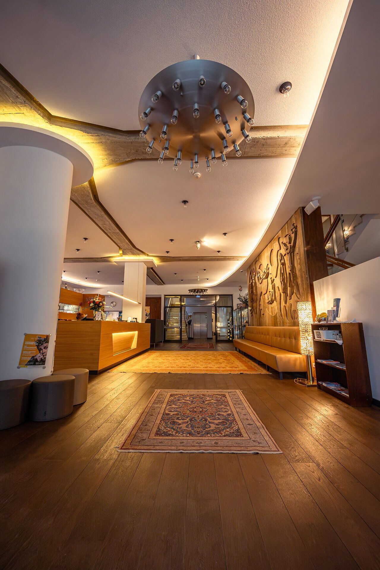 Der Empfangsbereich des Hotels strahlt eine einladende Atmosphäre aus, die durch warmes Licht und stilvolle Einrichtung ergänzt wird. Die harmonische Verbindung von modernem Design und gemütlicher Eleganz lädt dazu ein, sich sofort wohlzufühlen und die Annehmlichkeiten des Aufenthalts zu genießen.