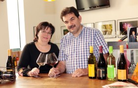 Ein Mann und eine Frau stehen an einem Tisch mit Weingläsern und Weinflaschen.
