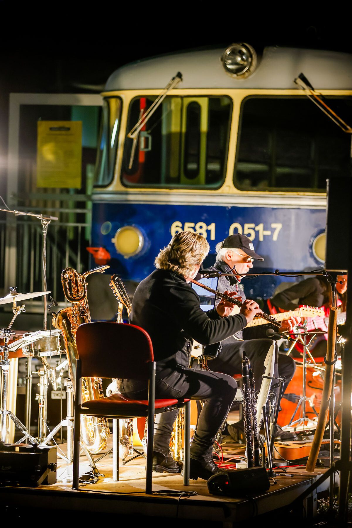 In der warmen Abendluft erklingen sanfte Melodien, während Musiker auf einer kleinen Bühne ihre Instrumente spielen. Die stimmungsvolle Atmosphäre wird durch das nostalgische Ambiente des Kulturbahnhofs unterstrichen, wo die Klänge der Musik harmonisch mit dem Lichtspiel der Umgebung verschmelzen.