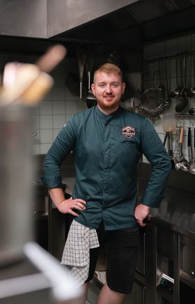 Thomas Reinisch steht in der Küche im Lokal Thomas im Johanneshof, blickt in die Kamera, Arme an die Hüfte gelehnt.
