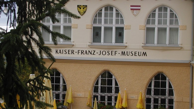 Fassade des Kaiser-Franz-Josef-Museums mit Fenstern und Wappen.