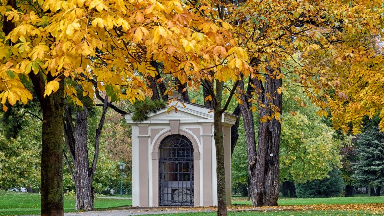 A small building in a park, surrounded by trees with yellow fall leaves.