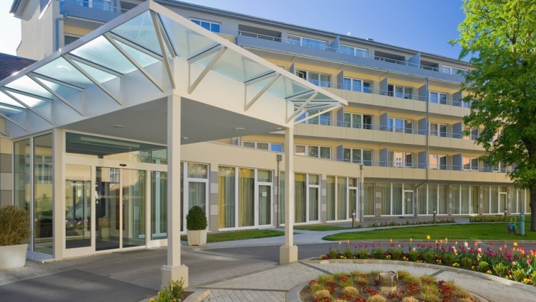 Moderner Gebäudeeingang mit Glasdach und Garten.