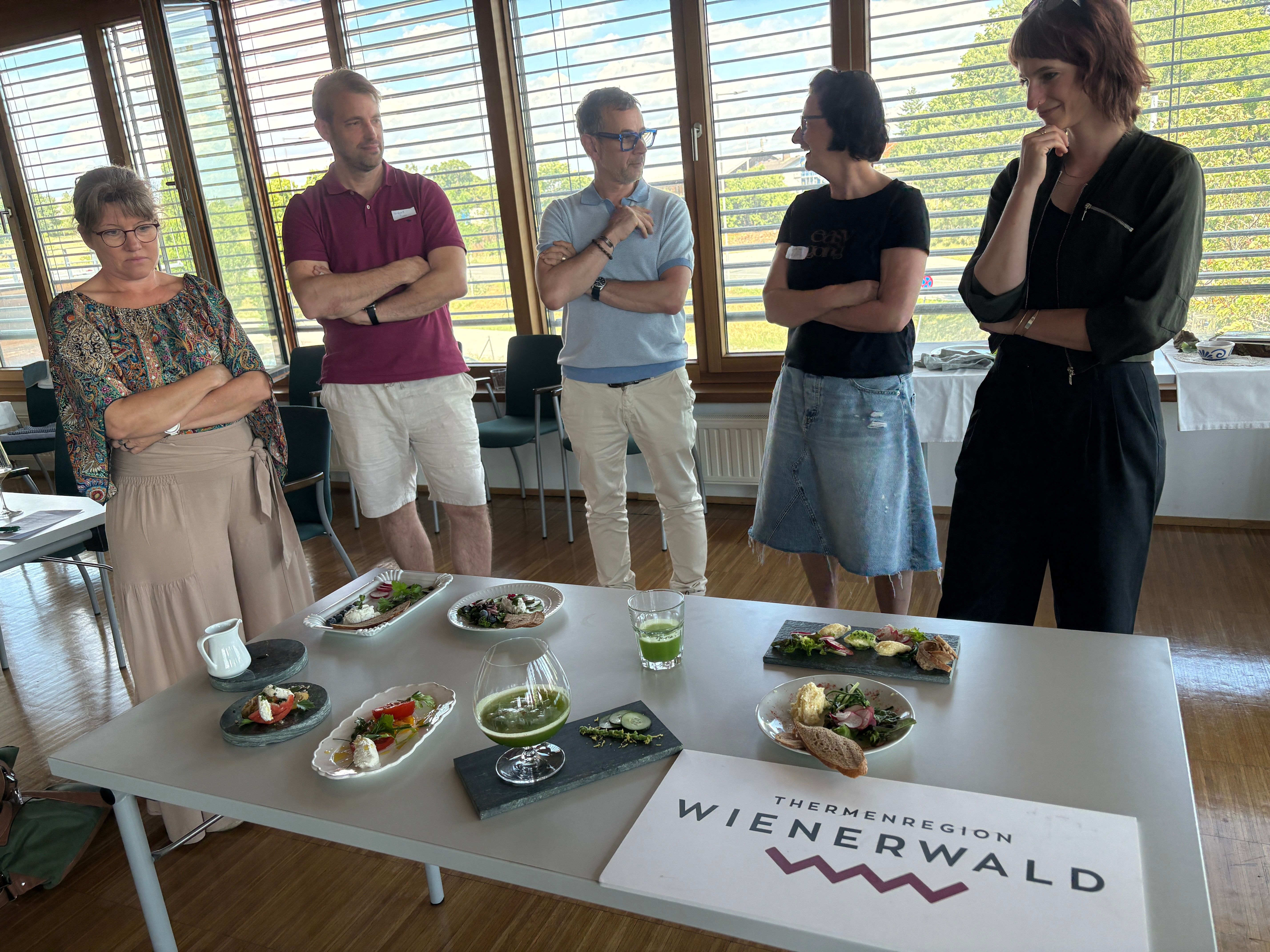 Gruppe steht vor einem Tisch auf dem Speisen kreativ zubereitet und dekoriert dargestellt werden.