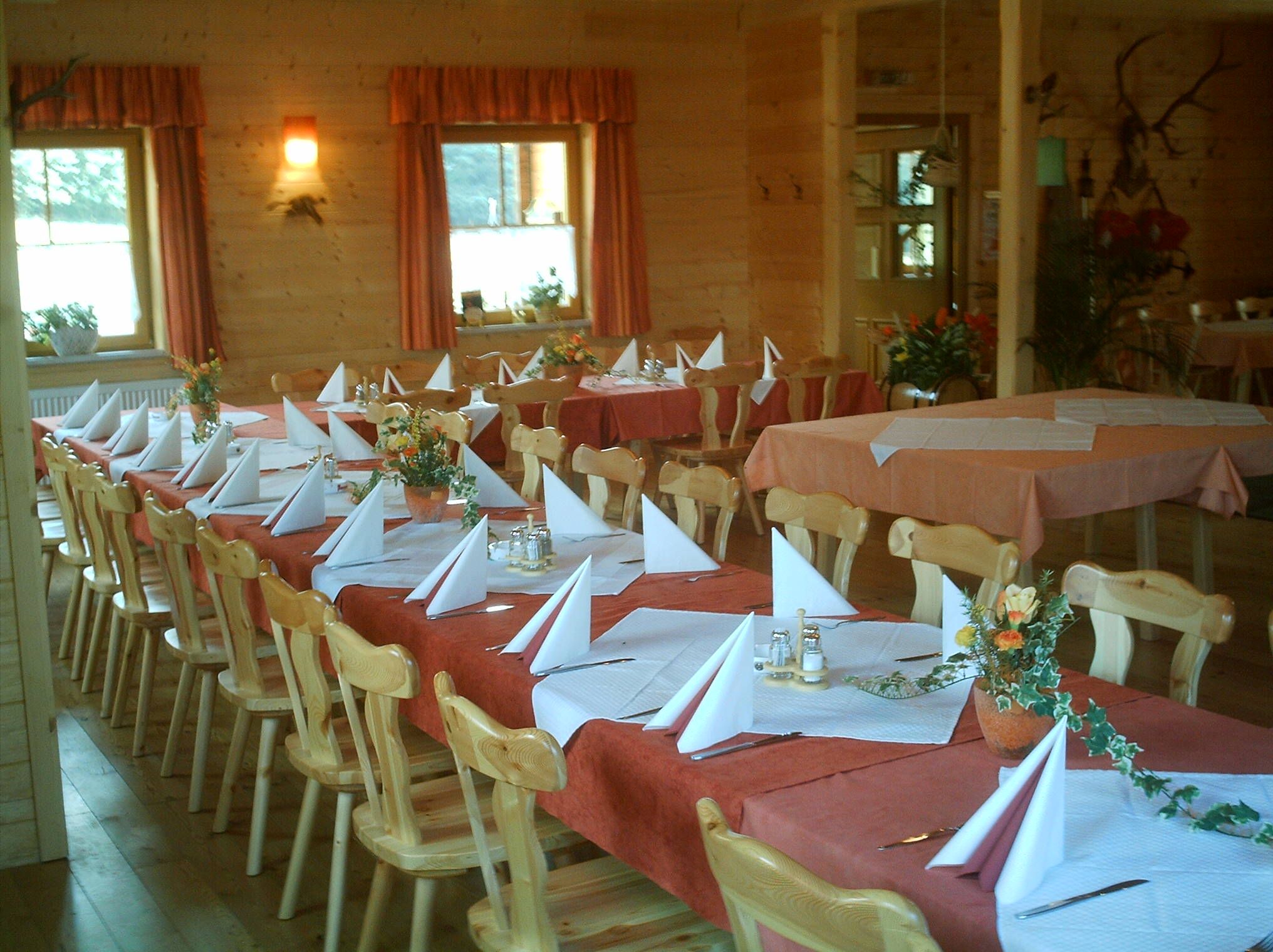 Ein rustikaler Gastraum mit Holzmöbeln, gedeckten Tischen und dekorativen Blumenarrangements.