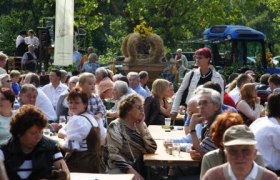 People sit at wooden tables at an outdoor party.