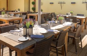 A terrace with wooden tables set with bottles of wine, glasses and lavender in pots.